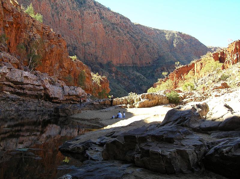 Ormiston.jpg - Bei Sonnenschein leuchten die hohen Felswände der Schlucht in verschiedensten Farben, was auf den unterschiedlichen Mineralien des Gesteins zurückzuführen ist.